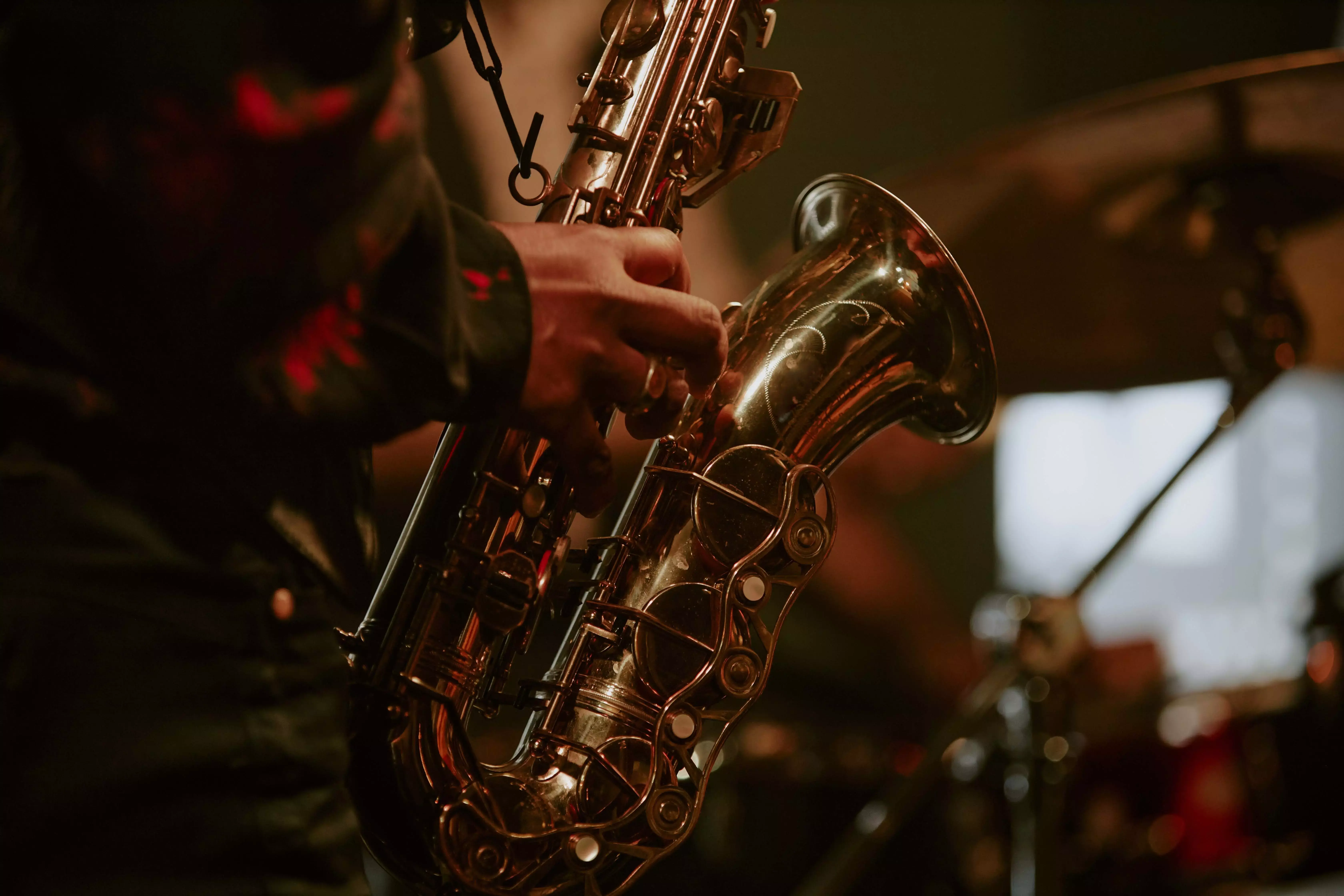 Close-up of a musician's hands playing a golden alto saxophone in a dimly lit setting